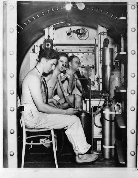 Dr. Edgar End, Max Gene Nohl and John Craig (the "human guinea pigs") are shown inside the decompression chamber located at the Milwaukee County Emergency Hospital in Milwaukee. The year is probably 1936. The three individuals are testing Dr. End's helium-oxygen mixture that would prove to extend the time underwater and the depth that divers could reach. As a result of these experiments, along with new self-contained dive gear they devised, Max Nohl was able to set a record deep dive in Lake Michigan on December 1, 1937.