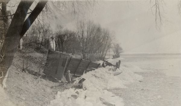 A child, possibly Richard "Dick" Lloyd Jones, stands near the wreckage of a wooden structure caused by ice break-up on Lake Monona.