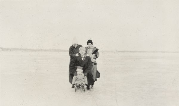 Two women stand behind Richard Lloyd Jones and son Richard Lloyd Jones Jr., who are seated on a sled on frozen Lake Monona.