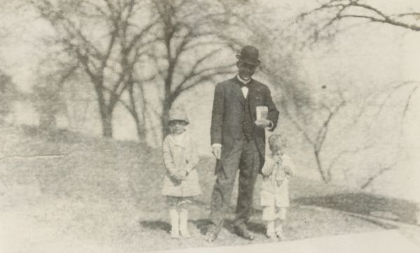 Booker T. Washington stands flanked by Richard "Dick" Lloyd Jones (left) and Jenkin Lloyd Jones (right) near the shore of a Madison lake.  Washington, described as a good friend of Rev. Jenkin Lloyd Jones, was in Madison in April 1914 for a speaking engagement and stayed with the Lloyd Jones family.