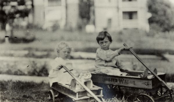 Richard "Dick" Lloyd Jones and his sister Florence Lloyd Jones (Bis or Bisser) each sit in separate coaster wagons.