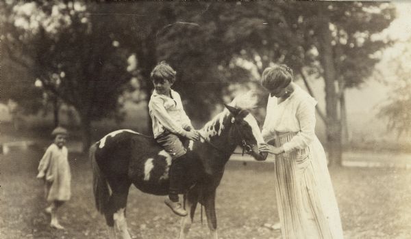 Jenkin Lloyd Jones sits on a pony calmed by his mother, Georgia Lloyd Jones.  His younger sister, Florence (Bis) is in the background.