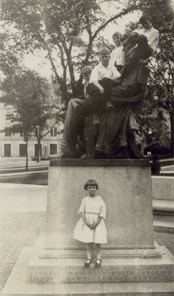 Florence (Bis) Lloyd Jones stands at the base of the Abraham Lincoln statue in front of Bascom Hall on the University of Wisconsin-Madison campus.  Her brother, Richard "Dick" Lloyd Jones, sits on Lincoln's shoulders; three other boys join him on the figure.  Birge Hall is visible in the background.  Photo taken after the dedication of the Lincoln Terrace in June 1919 featuring the replica bronze figure of Lincoln created by Adolph Weiman.