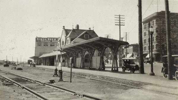 A view from the east end of the East Madison Chicago, Milwaukee & St. Paul railroad station, 501 East Wilson Street. Automobiles are parked along the curb and the Cardinal Hotel, 416-18 East Wilson Street, and other buildings in the 400 block of East Wilson Street are in the background.