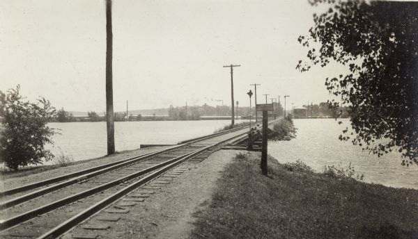 Looking southwest along the Chicago, Milwaukee & St. Paul Railroad causeway.  Two boys fish from the bridge.  The sign declares "Private Property.  No Thoroughfare.  Keep Off."  The Chicago & North Western Railroad track is in the background.