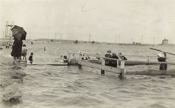 People swimming and diving in Monona Bay near the Brittingham Park bath house.  The railroad causeway is in the background.