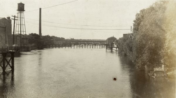 Elevated view of the Rock River, with a large smokestack and water tower on the left.  Richard Lloyd Jones was born in Janesville in 1873 and lived there until his father, Rev. Jenkin Lloyd Jones, moved to Chicago in 1881.  This picture was taken when Richard moved his family from Madison to Tulsa, Oklahoma, in 1919. There is a sign on a raft in the river near the shoreline on the right which says: "New Method Shoe Parlor Saves You Money".