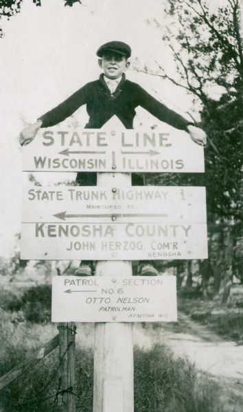 Richard "Dick" Lloyd Jones standing on the state line sign between Wisconsin and Illinois.  This picture was taken when the Lloyd Jones family moved from Madison to Tulsa, Oklahoma, in 1919.