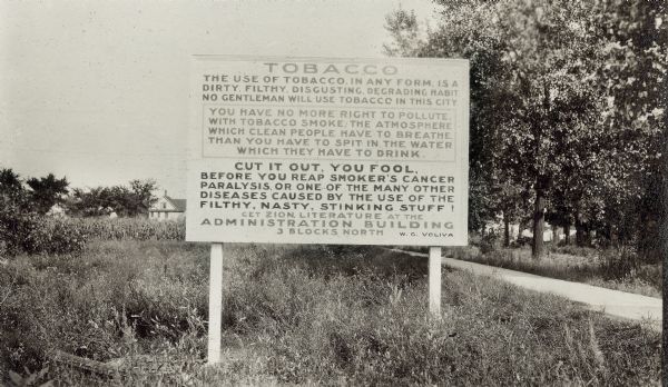 Road sign in field, stating that: "No Gentleman Will Use Tobacco in This City," and "Cut It Out You Fool."  Photo taken by the Richard Lloyd Jones family during their move from Madison to Tulsa, Oklahoma and identified in scrapbook as "Zion City Gospel"