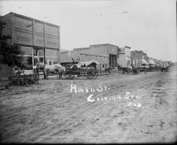 Main Street in Coloma with dirt road and horse-drawn wagons.