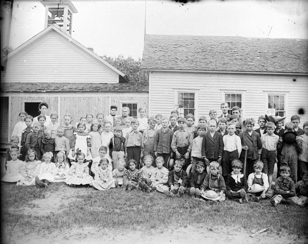 Exterior view of large group of children posed in front of their school.