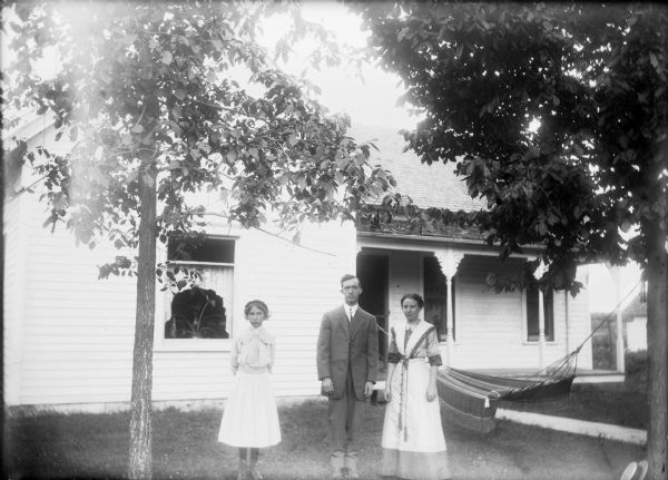 Otto Lindner home with (left to right), unidentified woman, Otto and Grace Lindner standing in front of hammock.