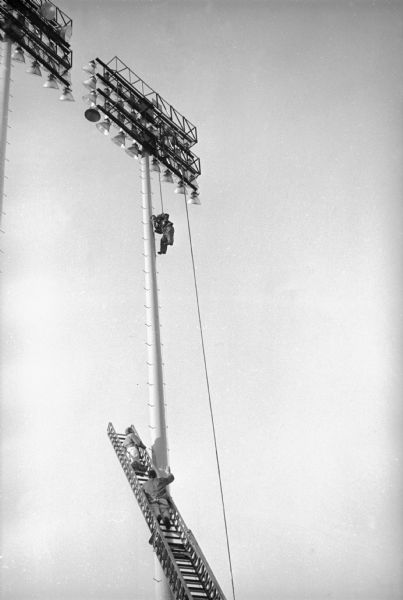 Milwaukee County Stadium on the day of the first game of the 1958 World Series, between the Milwaukee Braves and the New York Yankees. A man is being lowered from the stadium lights by fire fighters on a fire engine's ladder.