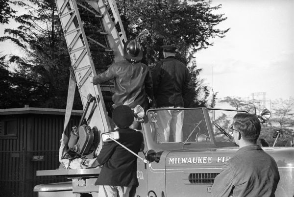Milwaukee County Stadium on the day of the first game of the 1958 World Series, between the Milwaukee Braves and the New York Yankees. Fire fighters and police officers at the base of a fire engine ladder, retrieving a man from atop one of the stadium's lighting platforms.