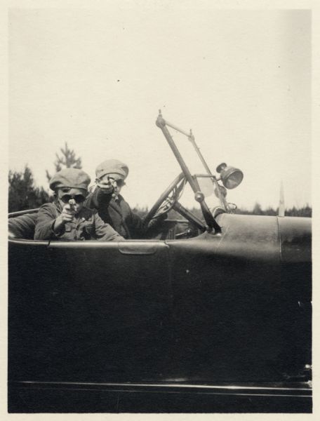 Two young boys sitting in a car wearing hats and sunglasses, play cops and robbers. One of the boys is thought to be Reginald Jackson, Jr., of Madison. Apparently portraying the robbers, they are both pointing their weapons at the camera.