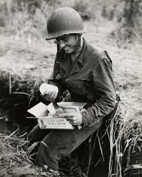 Corporal Frank Abrashinsky of Sheboygan, somewhere in New Guinea,  opening his Red Cross Christmas package.