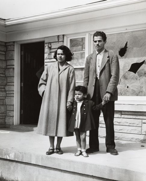 Andrew Wade and his wife and daughter stand in front of their house. Their front windows have been damaged by rocks and rifle shots.
