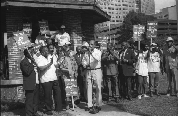 Richard Arrington, Jr. (at the microphone), the first black to be elected mayor of Birmingham, speaks to a re-election rally.  Among the supporters applauding are Gordon Spivey (to the left) and Rev. Fred Shuttlesworth (to the right), the president of the Southern Organizing Committee (SOC).