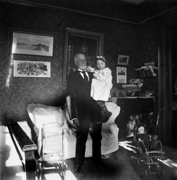 An elderly man stands in a room holding a small girl. Caption on negative reads, "Mary C. and Grandpa."