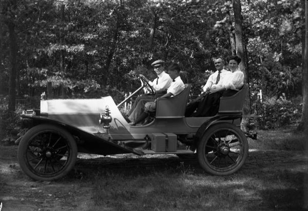 Four individuals sit in four-seat runabout parked in a wooded area.