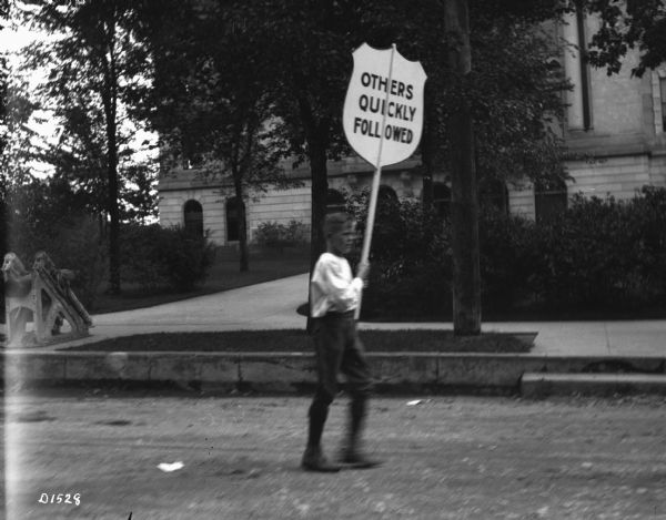 A boy parades past the Oneida County courthouse with a sign that reads, "Others Quickly Followed."