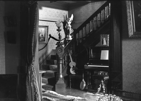 An interior view of the Ada Meinhardt residence. There is an elaborate stairway with several musical instruments displayed below.
