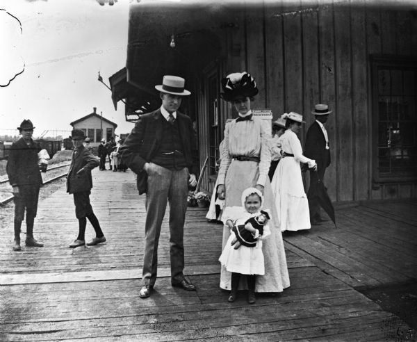 The J.B. Alexander family at the Wisconsin Central train depot. The young child in front holds a doll.
