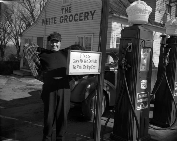 A gas station attendant puts on his coat outside the White Grocery and Filling Station in Madison. A sign near the pumps reads, "Please Give Me Ten Seconds To Put On My Coat."