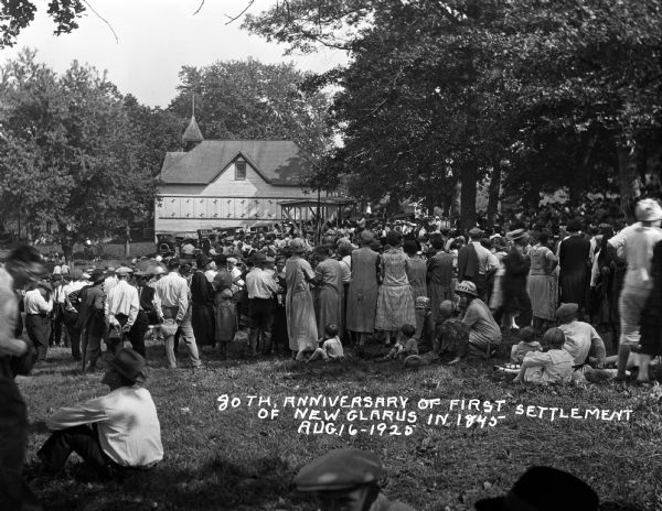 A large crowd of men, women, and children gathers outdoors to celebrate the 80th anniversary of the Swiss settlement in New Glarus.