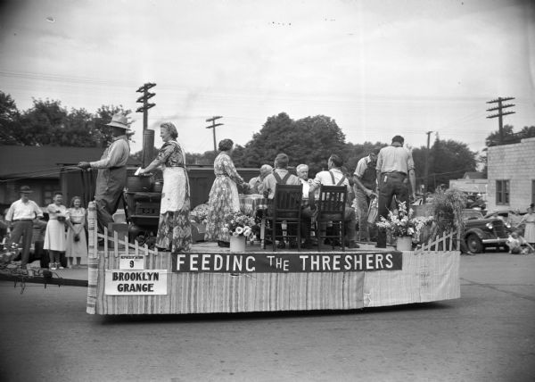The Brooklyn Grange parade float in a Labor Day parade. Men and women on the float mimic various household and recreational activities.