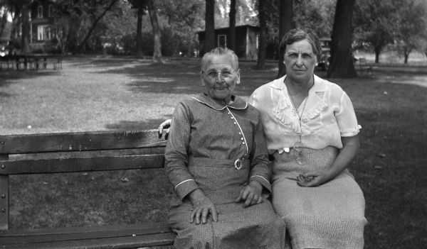 Two women sit on a bench in a park. Caption reads "Aunt Lydia with the photographer's wife Mary."