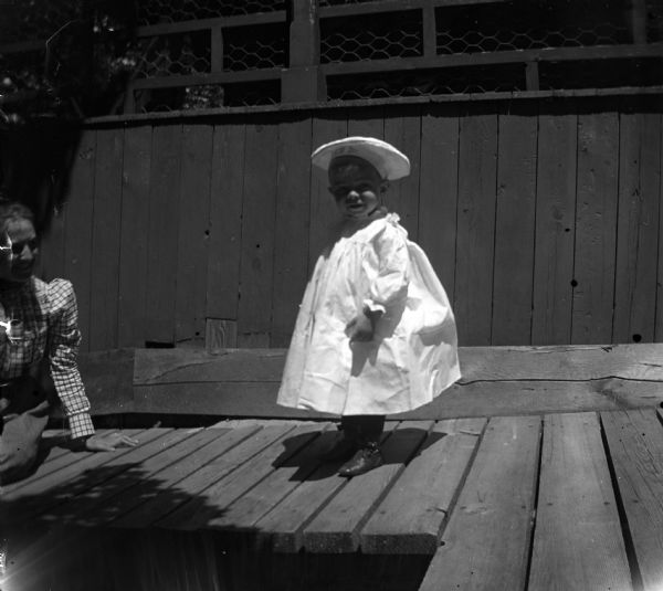 Caption reads, "Sam D. Conant at cottage." A woman sits on the boardwalk and looks at the child.