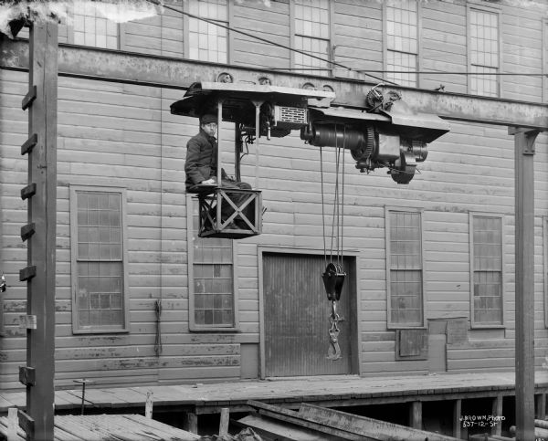 Exterior view of a Pawling & Harnischfeger monorail hoist with the operator sitting in the cab. The text on the lower right reads "J. Brown, Photo 537-12-St" and very likely is Milwaukee photographer Joseph Brown, 537 12th Street.
