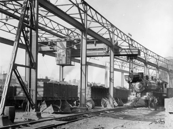 Double extension gantry crane with a grab-bucket at the Pennsylvania Railroad Co. The crane is stamped with the text "Pawling & Harnischfeger Builders, Milwaukee, Wis., Capacity 8,000 Lbs., No. 588." while the locomotive on the right is numbered 1539.