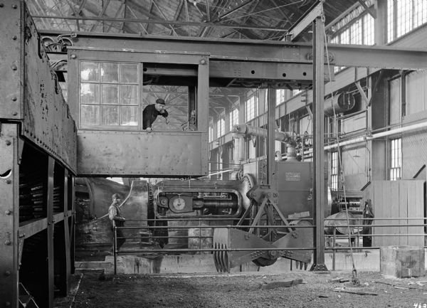 Pawling & Harnischfeger monorail hoist with a 3-ton grab bucket in the engine room of the Wisconsin Steel Co., which was a subsidiary of the International Harvester Company. The machinery to the right is stamped "Built By the C.G. Cooper Co., Mount Vernon, Ohio, USA." There is a man in the cab of the crane as well as one standing on the engine room floor.