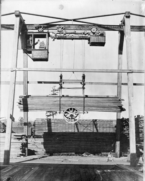 Pawling & Harnischfeger monorail hoist crane with lumber handling unit outdoors. A man is in the cab, which is stamped "Pawling & Harnischfeger, Milwaukee, Wis."