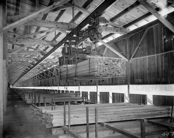 Pawling & Harnischfeger monorail hoist with lumber handling unit inside of an unidentified lumber warehouse. There is a man operating the unit.