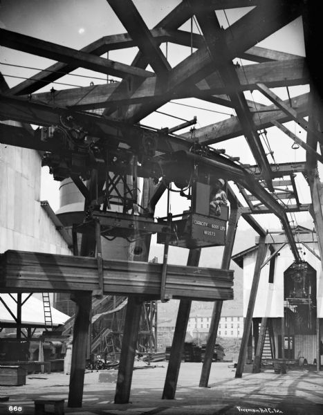 Pawling & Harnischfeger 3-ton monorail hoist in a lumber mill with a man in the cab. Text stamped on cab reads "Capacity 6,000 Lbs., No. 2573." In the lower right corner, the photograph is signed "Freeman Art Co. Foto."
