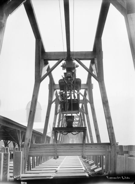 Pawling & Harnischfeger monorail hoist crane handling lumber with a man in the cab operating the crane. In the lower right corner, the photograph is signed "Freeman Art Co. Foto."