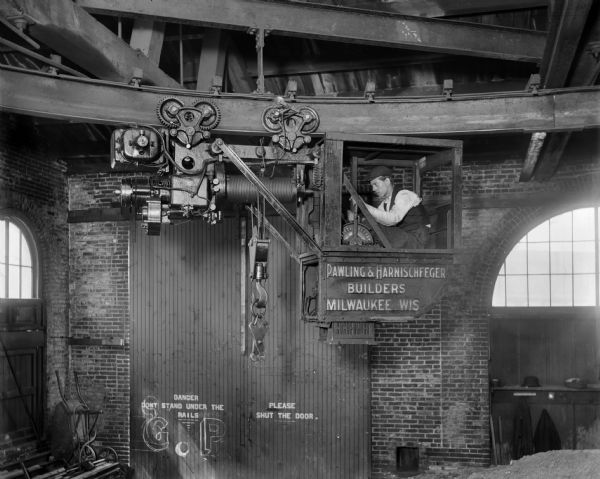 Pawling & Harnischfeger 2-ton monorail hoist in the William Wharton Jr. & Co. rail storage house. There's a man in the cab and the text on the cab reads "Pawling & Harnischfeger Builders, Milwaukee, Wis."