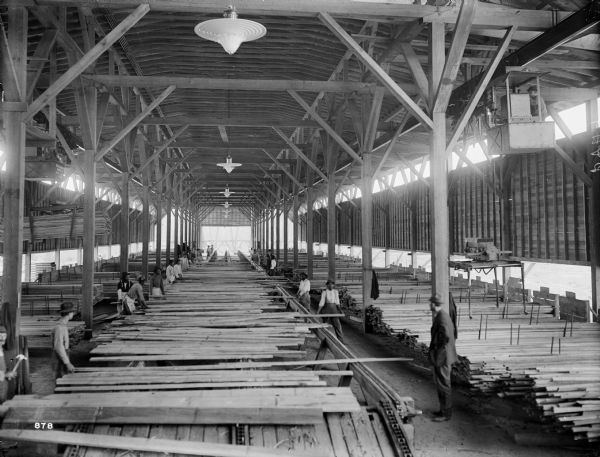 Pawling & Harnischfeger 3-ton monorail hoist in a lumber mill. There is an operator in the cab, and many men working on the floor of the mill.