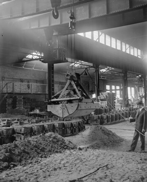 Pawling & Harnischfeger single line grab bucket in an unknown foundry. There is a man in a suit and tie and wearing a cap, who is holding the rope attached to the bucket. The crane is stenciled "No. 343."