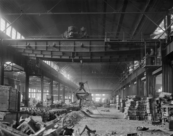 Pawling & Harnischfeger 3-ton grab bucket suspended from a 25-ton type  "AN" crane with a 5-ton auxiliary type "A" trolley in an unidentified foundry. A man in the upper right is operating the crane, which is stamped "Pawling & Harnischfeger Builders, Milwaukee, Wis., Main Hoist 50,000 Lbs., Auxiliary 10,000 Lbs., No. 1491." A boxcar in the background reads "C.M.&S.P."