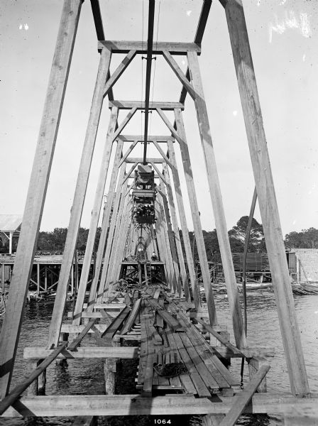 Pawling & Harnischfeger 5-ton monorail hoist and track running over a body of water presumably to load a boat with lumber from a lumber yard. There is a man in the cab, as well as a man on the dock. The location is possibly Pensacola, Florida.