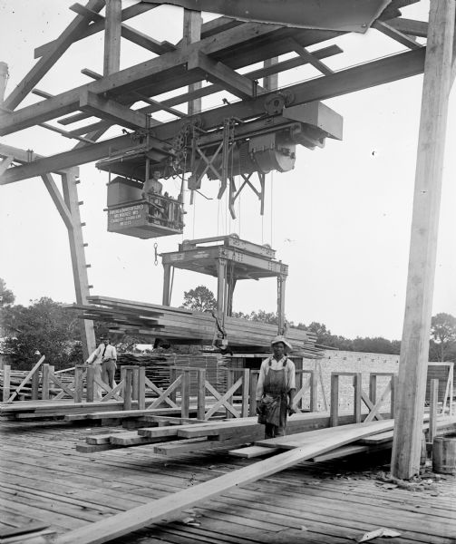 Pawling & Harnischfeger 5-ton monorail hoist with lumber handling unit on a loading dock, possibly in Pensacola, Florida. There is a man in the cab, as well as men standing on the ground.