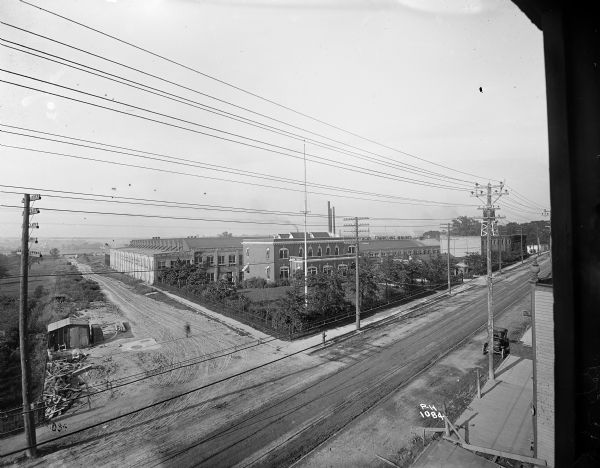 Elevated view from window of the Pawling & Harnischfeger factory on the corner of National Avenue and 44th Street. The road in front has power lines along it, an automobile is parked on the right. A sign on a roof says "[obscured]feger Traveling Cranes."