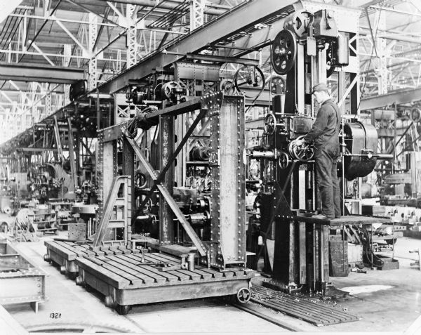 A horizontal hole boring drill, presumably at the Pawling & Harnischeger factory, drilling holes into crane parts. There is a man on the lift operating the drill.