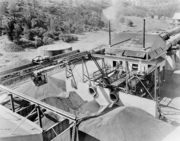Elevated view of Milwaukee Electric Crane & Manufacturing Company grab bucket crane on the exterior of the Calaveras Cement Factory. A sign on the crane reads "The Milwaukee Crane" and the crane is stamped "Milwaukee Electric Crane & Mfg. Co., 8 Tons, No. 736." This is reportedly one of two grab bucket cranes in the factory.