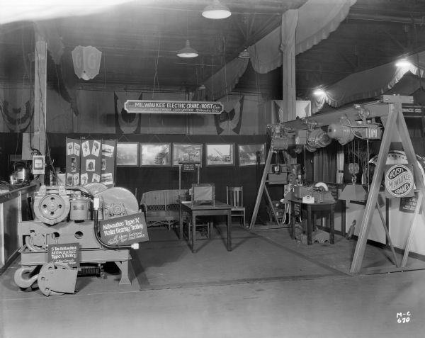 Various Milwaukee Electric Crane & Manufacturing Company crane parts and other products are on display at the factory's sales floor. Signs read "Milwaukee Electric Crane & Hoist Corp. Division of Harnischfeger Corporation, Milwaukee, Wis." "Milwaukee Single Line Foundry Bucket," "Milwaukee Type "A" Roller Bearing Trolley, All Gears Enclosed, Safety Type Limit Switch" and "5 Ton Bottom Block Milwaukee Type "A" Trolley 5 Ton Capacity."