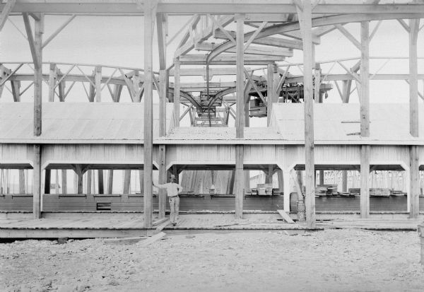 A man wearing a wide brimmed hat leans on a support beam underneath a 3-way switch at the Madero Lumber Company. A P&H handling unit (No. 2821) is also visible.